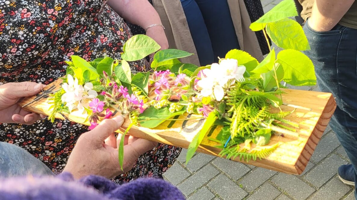 Iemand houdt een houten plant vast met kruiden en bloemen uit eigen tuin daarop.