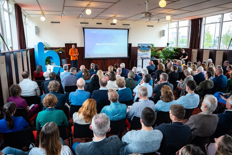 Een zaal vol met mensen kijkt naar een presentatie tijdens het Samen sterk met buurkracht evenement.