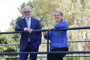 Burgemeester Gerard van den Hengel en opgavemanager Linda Sijm van gemeente Opmeer leunen op een railing en kijken lachend naar de camera.