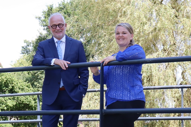 Burgemeester Gerard van den Hengel en opgavemanager Linda Sijm van gemeente Opmeer leunen op een railing en kijken lachend naar de camera.