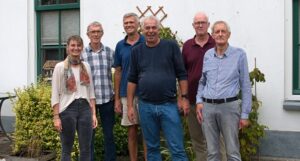 Vijf leden van de initiatiefgroep Zegveld poseren samen met Buurkracht buurtbegeleider Jos voor een wit huis met planten op de achtergrond.