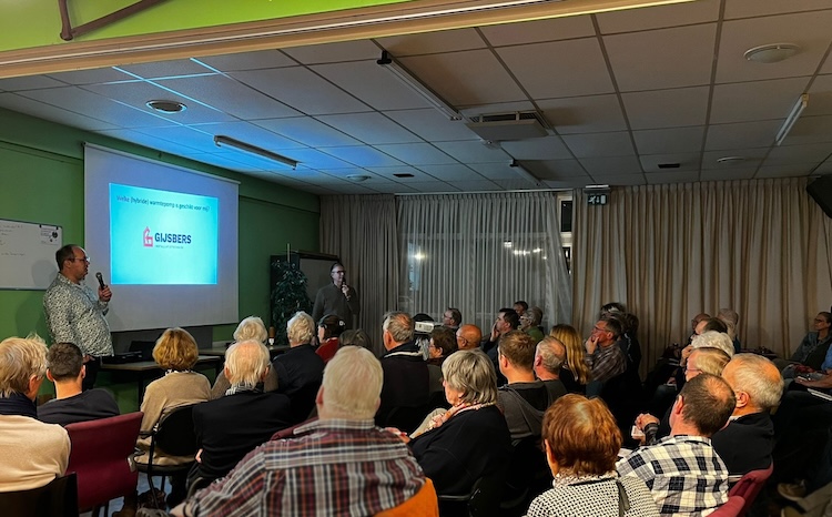 Een groep mensen zit in een ruimte en kijken naar een presentatie op een beamerscherm.