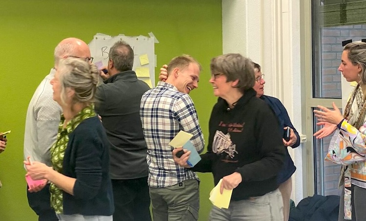 Een groep mensen staan en lopen in een ruimte. Ze praten met elkaar en hebben post-its vast.