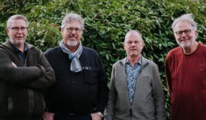 Vier leden van het buurtteam uit Kloetinge poseren voor een groene struik en kijken lachend naar de camera.