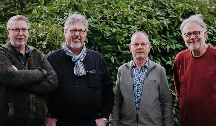 Vier leden van het buurtteam uit Kloetinge poseren voor een groene struik en kijken lachend naar de camera.