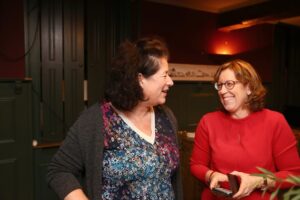 Twee mensen staan in een donkere, gezellige ruimte en kijken lachend naar elkaar.