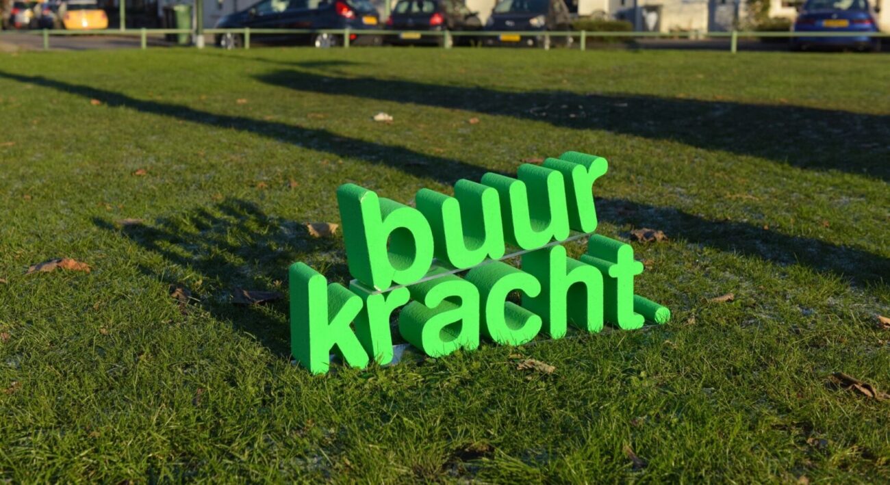 Groene 'Buurkracht' letters gemaakt van piepschuim staan in een grasveld.