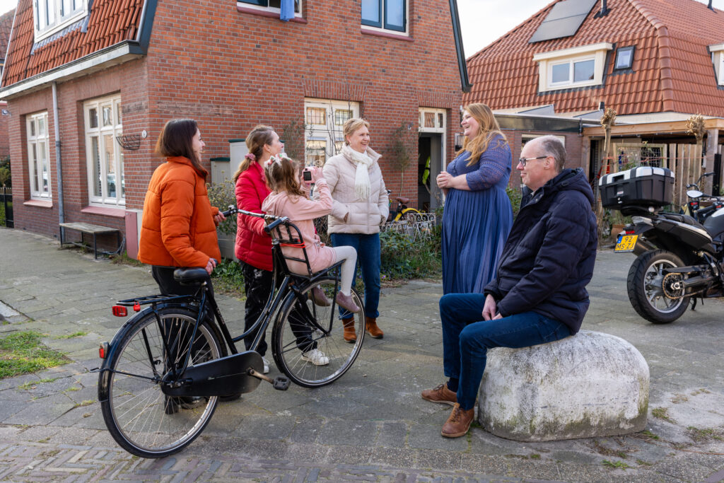 Vijf volwassen buren en één kind staan en zitten lachend te praten voor een huis in Utrecht Zuilen