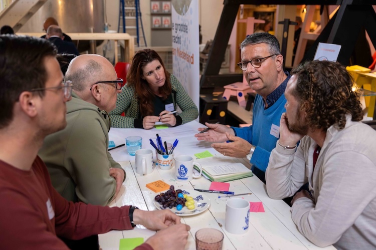 Een groep mensen zit rond een tafel tijdens het Samen sterk met buurkracht evenement. Op tafel liggen pennen, post-its en papier.