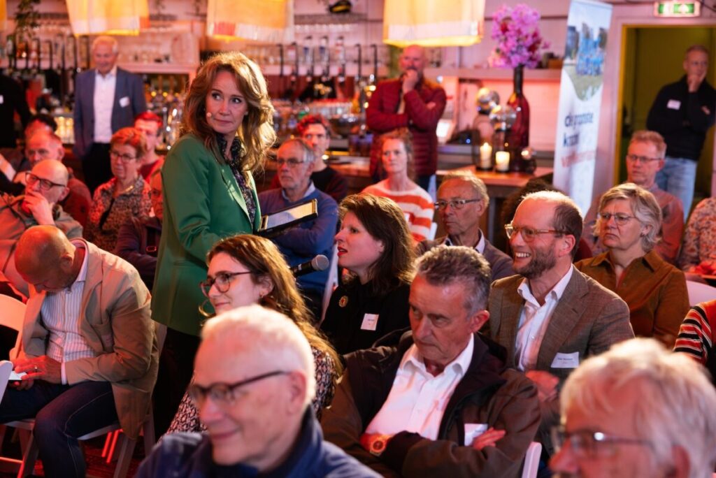 Helga van Leur stelt een bezoeker van het Samen sterk met buurkracht 2025 een vraag in een volle zaal met bezoekers.