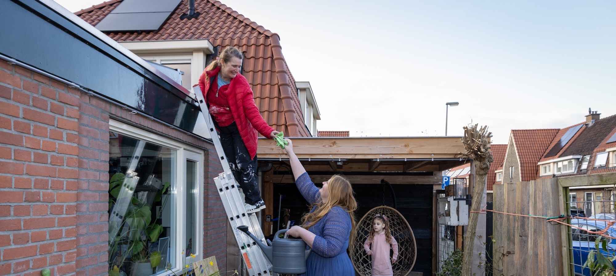 Een persoon staat op een lader en krijgt een spons aangereikt van iemand om het dak schoon te maken.