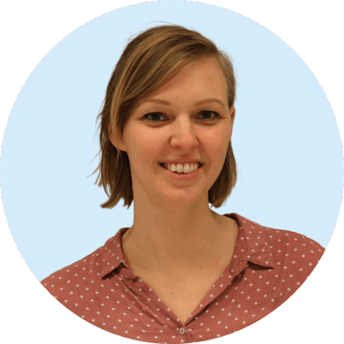 Portretfoto van Buurkracht buurtbegeleider Sabine, van schouders tot boven, genomen voor een lichtblauwe achtergrond.