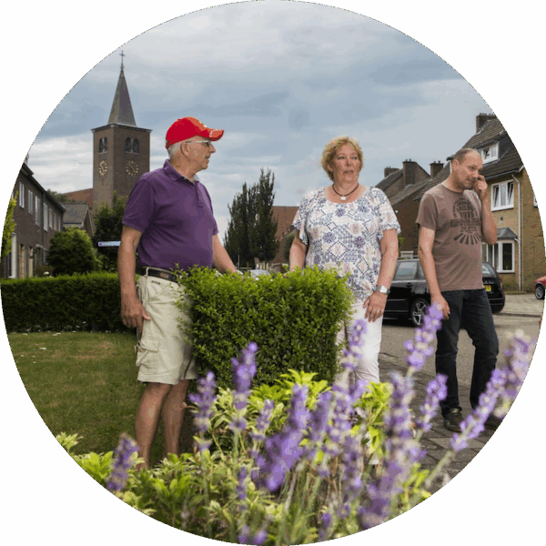 Drie mensen staan in een straat met lavendel op de voorgrond en een kerk en huizen op de achtergrond.